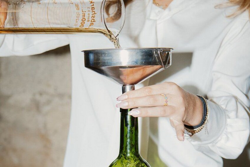 A person pouring a liquid from a measuring cup into a funnel attached to a green glass bottle. 5