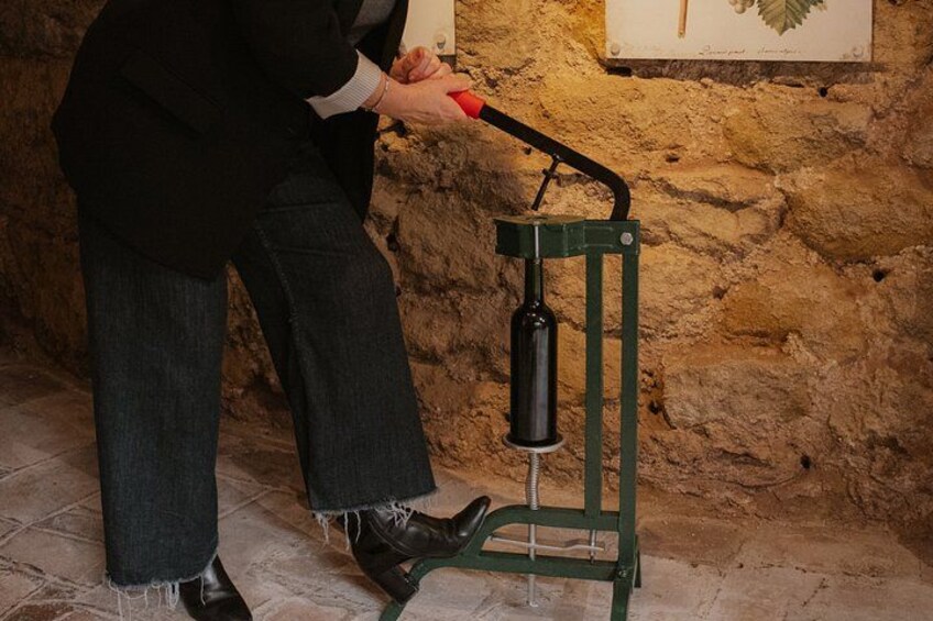 A person using a manual press with a green frame and a black cylinder, standing on a stone floor with a stone wall in the background. 3