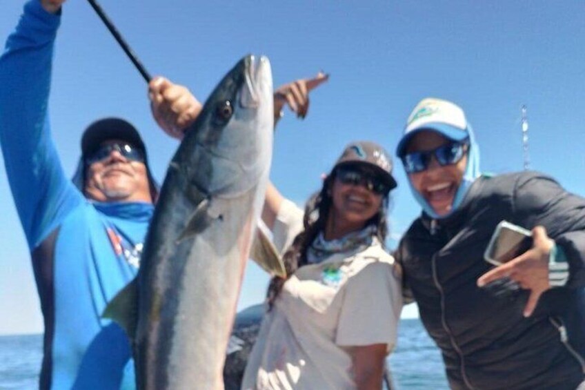 Three people holding a large fish, likely a salmon, on a boat with a clear blue sky in the background. 5