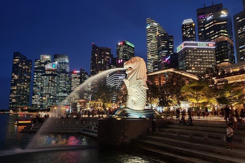 A cityscape with illuminated skyscrapers, a large dragon statue, and a fountain. 1