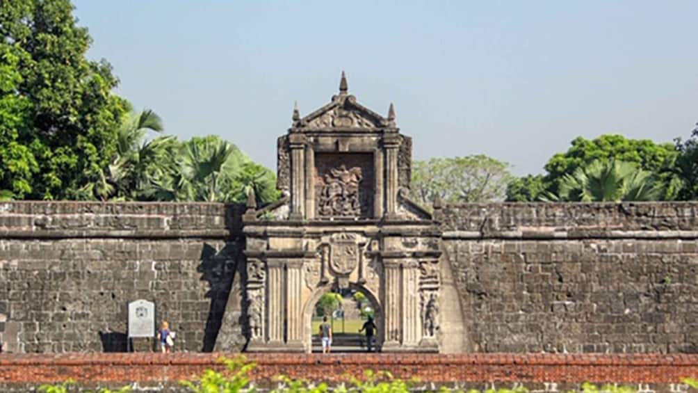 A historic stone gateway with intricate carvings and a central archway, surrounded by lush greenery and palm trees. 2