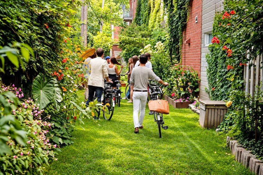 A group of people walking in a lush garden with bicycles. 4