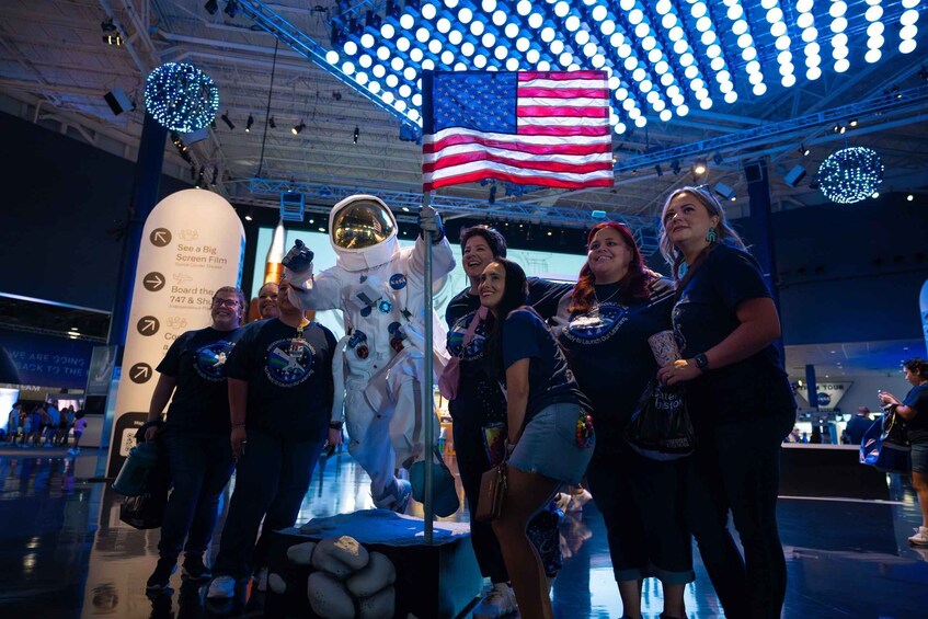 A group of people at a space exhibit with a large American flag and a space suit figure. 5