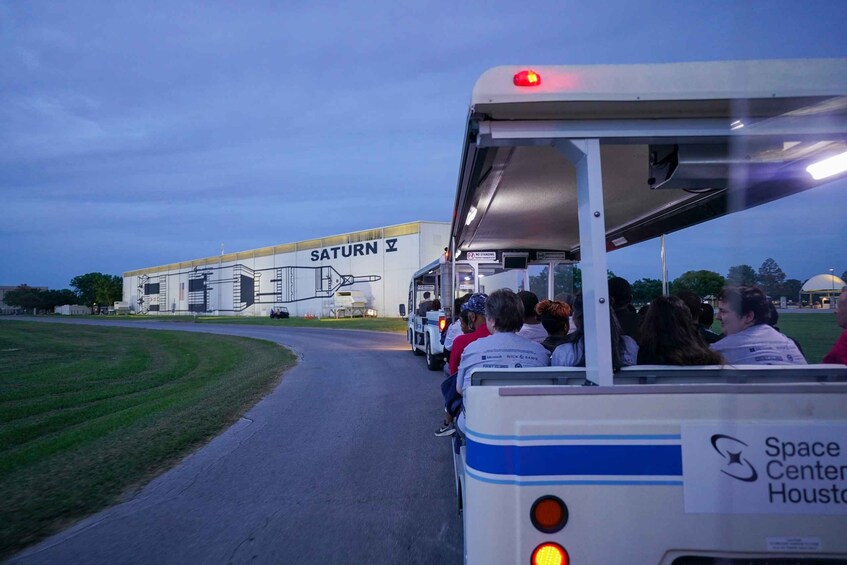 A tour bus with passengers approaching a building labeled "SATURN V". 2