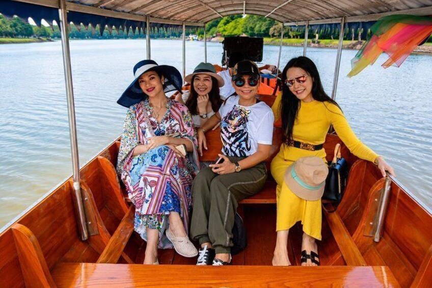 A group of people on a wooden boat with a canopy, surrounded by water and greenery. 4