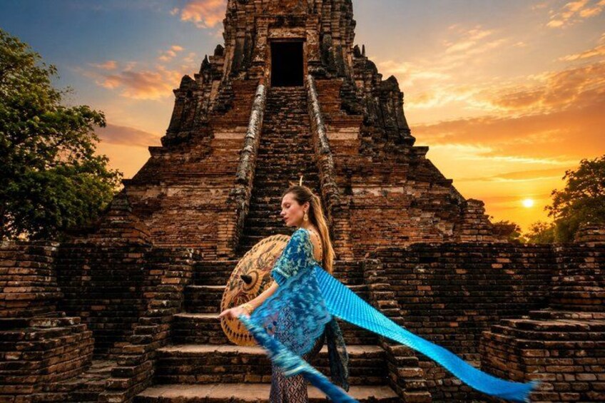A person in traditional attire with a blue garment and a large, ornate headpiece standing in front of an ancient brick temple structure. 2