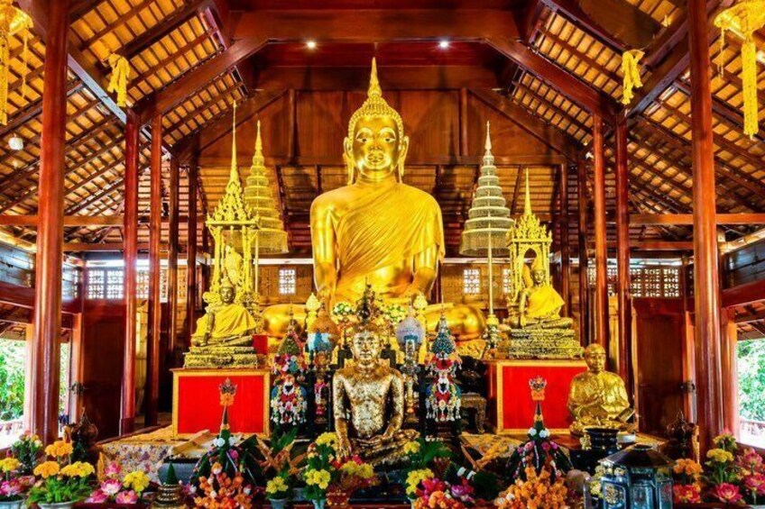 A large golden Buddha statue in a temple with smaller statues and offerings. 5