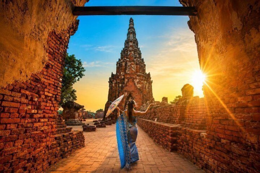 A person in traditional attire walking through an ancient brick pathway towards a temple with a sun setting in the background. 1