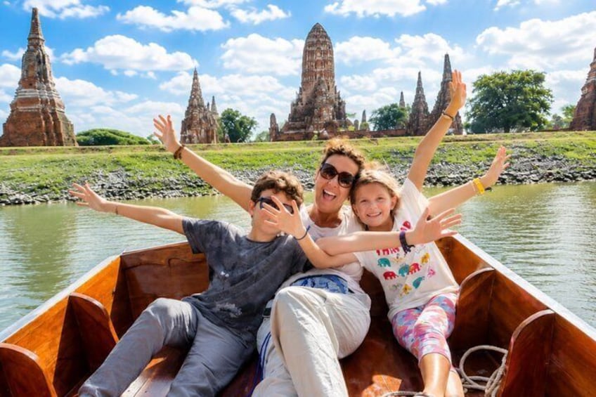 A family in a wooden boat on a river with ancient temple ruins in the background. 2