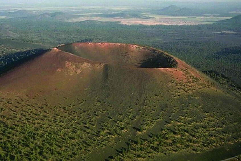A large, barren hill with a forested area in the foreground and a flat, open area in the background. 3