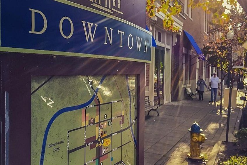 A street sign for 'DOWNTOWN' with a map below it, a fire hydrant, and a sidewalk with pedestrians. 1