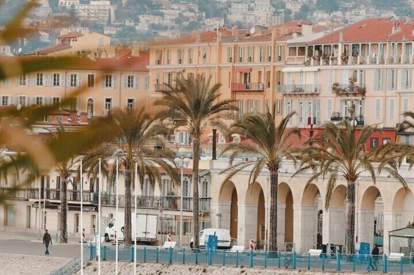A coastal promenade with palm trees, a blue fence, and buildings with balconies. 3
