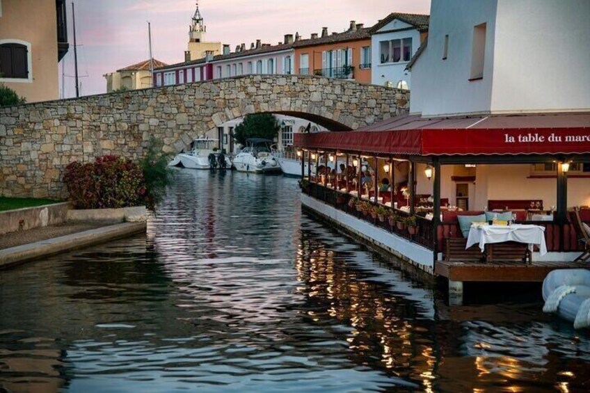A canal with boats, a stone bridge, and a restaurant named 'la table du mare' with outdoor seating. 1
