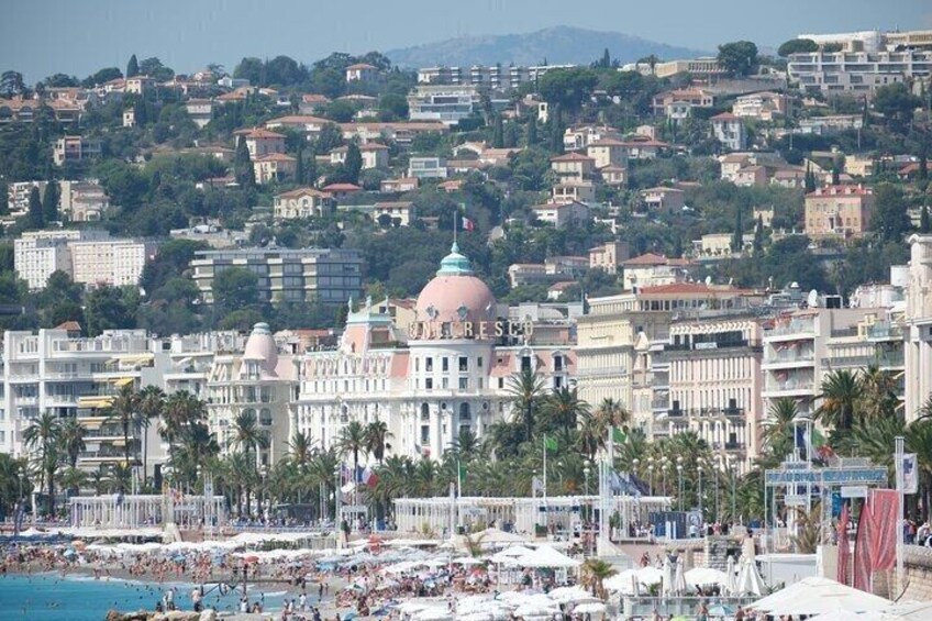 A coastal cityscape with a prominent building with a dome, palm trees, and a crowded beach. 2