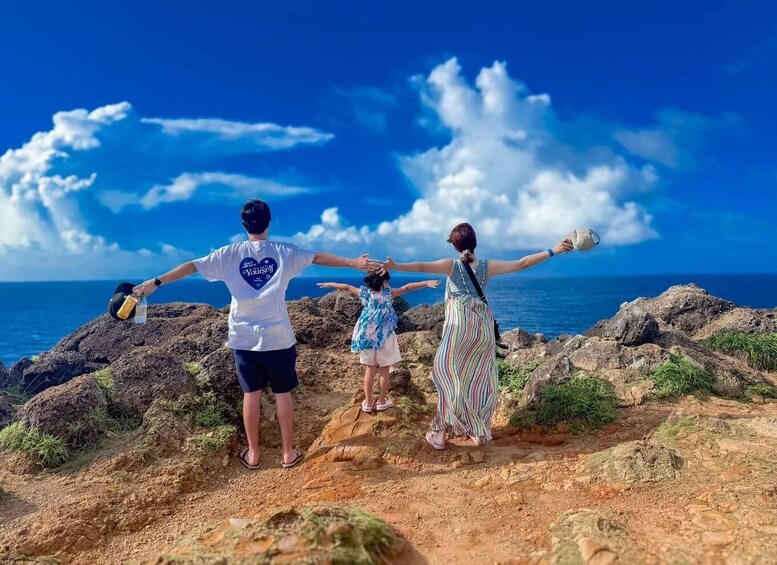 Three people standing on rocky terrain with a view of the ocean and sky. 1