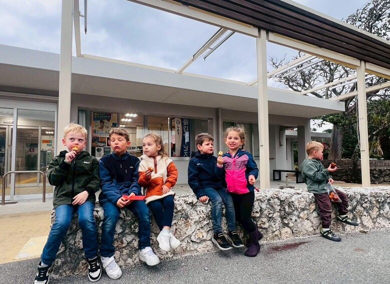 Children sitting on a stone wall in front of a modern building with large windows and a covered walkway. 5