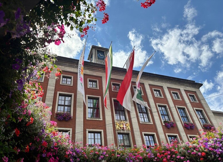 A building with multiple flags, a clear blue sky, and colorful flowers. 4