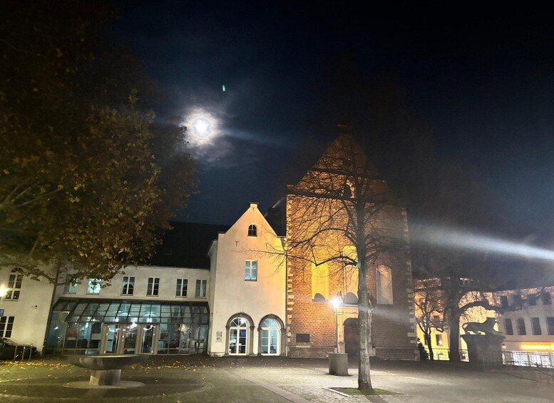 A night scene with a church illuminated by moonlight, a modern building with glass windows, and a tree in the foreground. 3