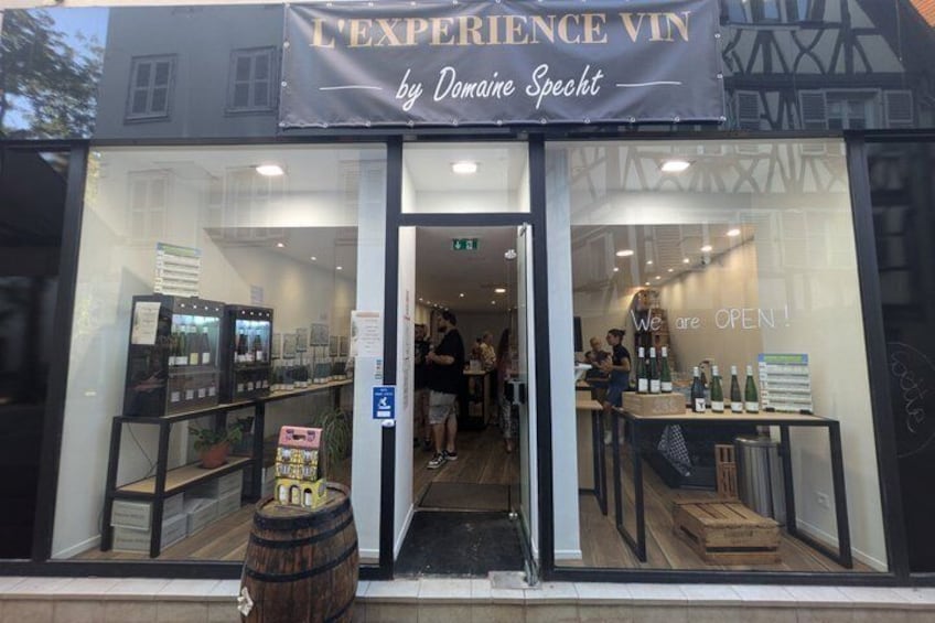 A storefront with a sign reading 'L'EXPERIENCE VIN by Danielle Specht' and a sign indicating the store is open. 2