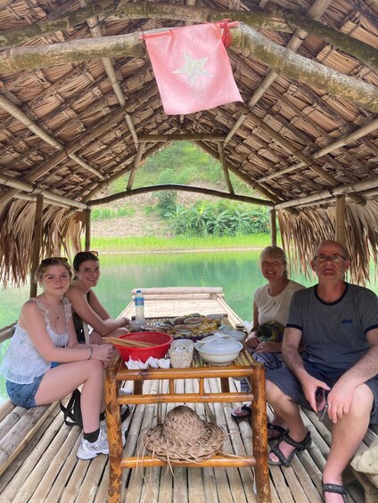 A group of people on a bamboo boat with a thatched roof, surrounded by water and greenery. 4
