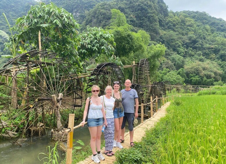 A group of people standing on a wooden bridge over a river, surrounded by lush greenery and bamboo structures. 5