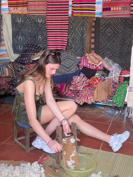 A person sitting on a stool, working with a wooden frame and a basket filled with wool. 2