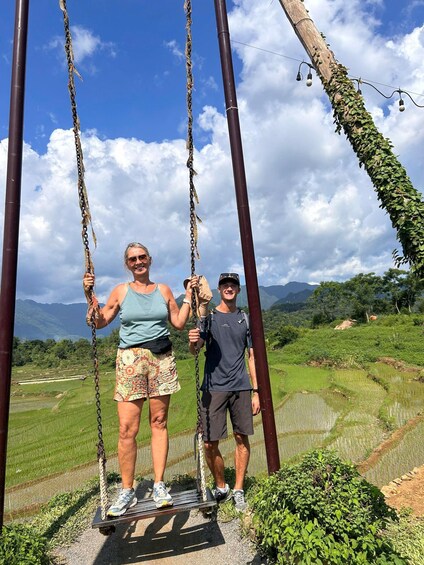 Two people on a swing set with a rural landscape in the background. 3