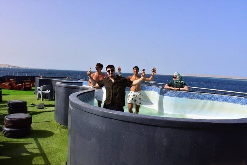 A group of people around a hot tub on a rooftop with a view of the sea. 2