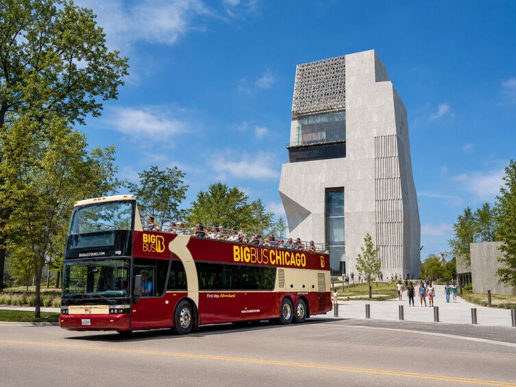 Un autobús de dos pisos con la inscripción 'BIG BUS CHICAGO', estacionado frente a un edificio moderno con una fachada singular. 1