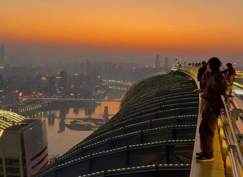 A curved pedestrian bridge with lights, overlooking a cityscape at sunset. 4