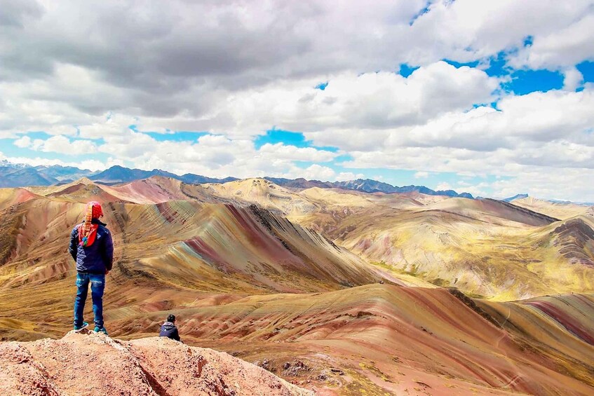 A person standing on a rocky outcrop overlooking a colorful mountain range. 4