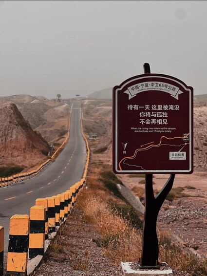 A road with a guardrail, a signboard with a map, and a barren landscape. 4