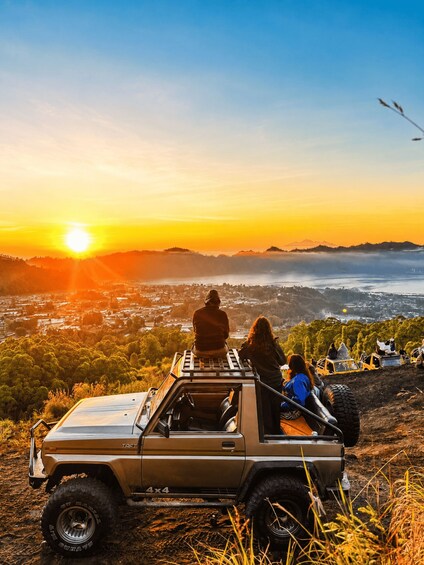 A 4x4 vehicle parked on a hill overlooking a valley with a sunset in the background. 2