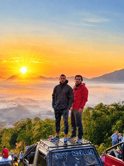 Two people standing on a vehicle with a sunset in the background. 3