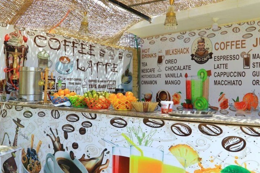 A coffee shop counter with a variety of coffee and tea options, a milkshake, and a selection of fruits and pastries. 5