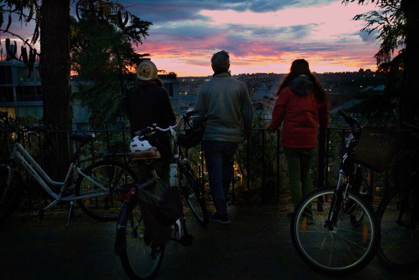Tre personer går längs en stig med cyklar, och de har utsikt över en stadssiluett i solnedgången. 4