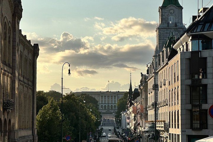 En stadsgata med historiska byggnader, ett klocktorn och en stor byggnad i bakgrunden. 1