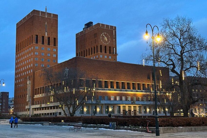 En stor byggnad av tegel med ett klocktorn, omgiven av träd och ett snötäckt område. 4
