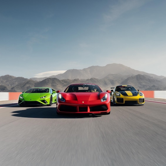 Three sports cars on a racetrack with mountains in the background. 1