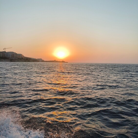 A sunset over a calm sea with buildings on the shore. 2