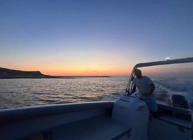 A person on a boat during sunset with calm water and a distant shoreline. 1