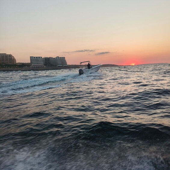 A boat moving across a body of water with a sunset in the background and buildings on the shore. 3