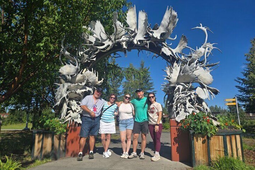 A group of people standing under a large antler sculpture. 1