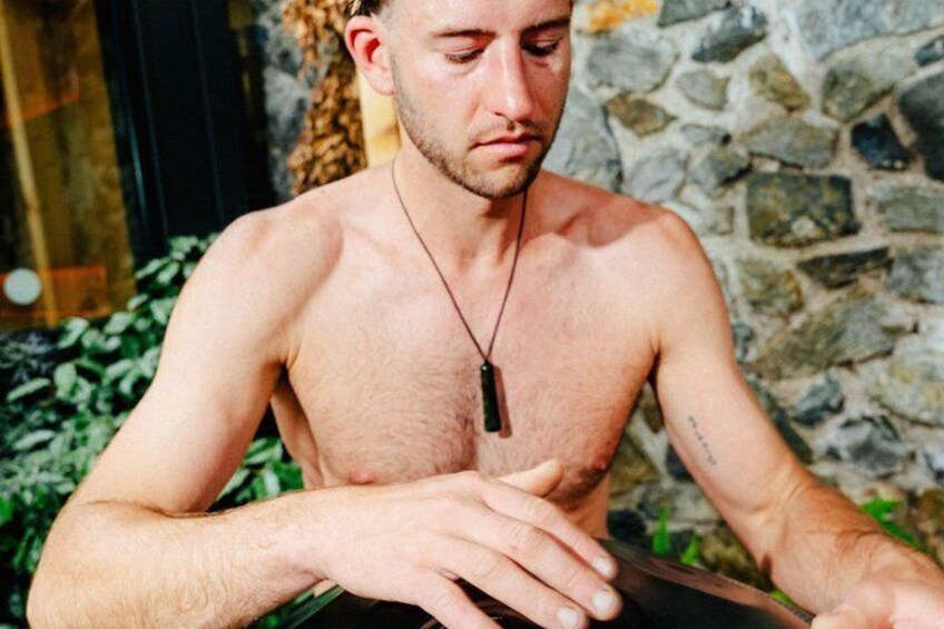 A shirtless man with a pendant necklace sitting at a table outdoors. 5