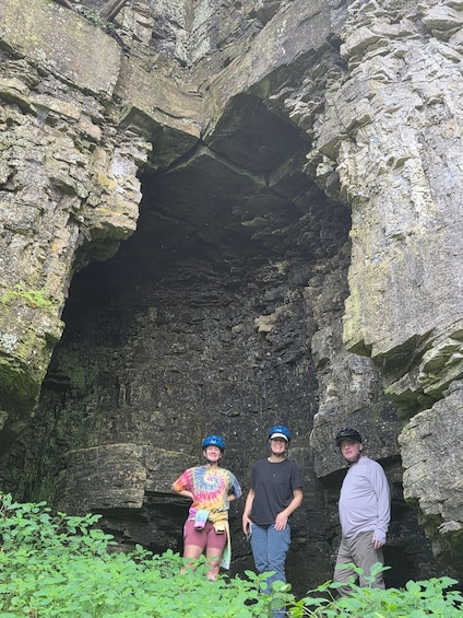 Three people standing in front of a rocky cave entrance. 3