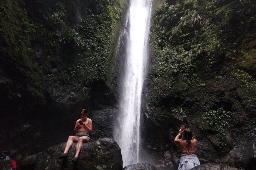 A waterfall, two people sitting on rocks, and lush greenery. 4