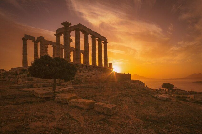 Ancient ruins with columns, a tree, and the sun setting over the landscape. 1