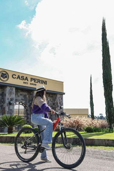 A person riding a bicycle in front of a building with a sign that reads 'CASA PERINI EST. 1929'. 3