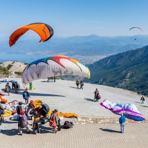 A group of people preparing for paragliding on a mountain with colorful paragliders and a clear sky. 2