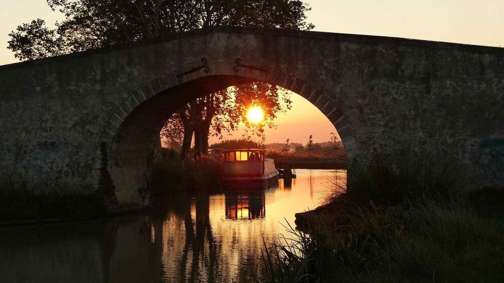 A stone bridge over a calm river at sunset with a boat in the water. 4
